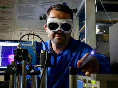 Miftar Ganija, wearing goggles investigates short pulsed laser systems in the lab.