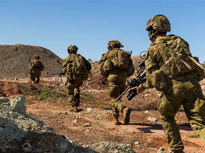 A photo of soldiers running over rough terrrain.