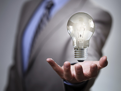 The torso of a man in a suit, holding up a lightbulb.