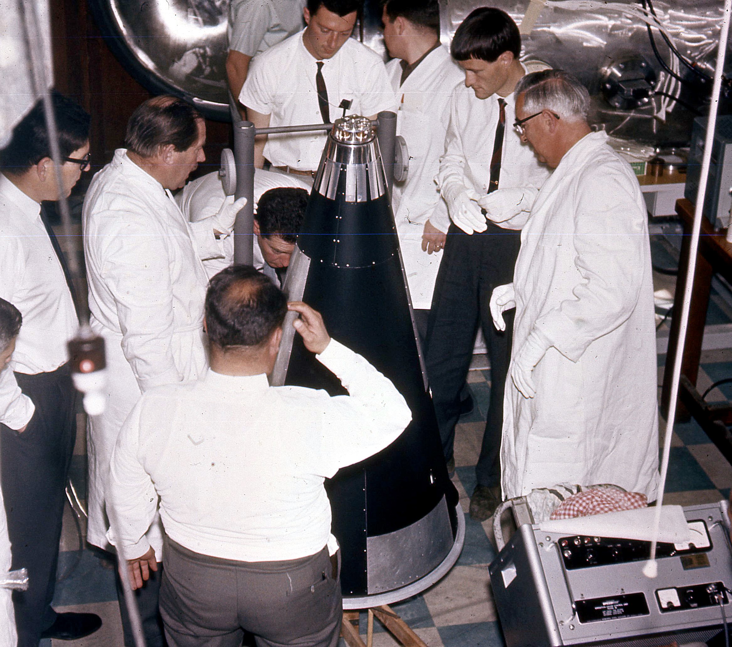 Inspecting WRESAT at the Department of Physics, University of Adelaide. To the immediate left of the satellite are Mr Bryan Rofe (WRE) and Prof. John Carver (University of Adelaide) and team leaders of the WRESAT project. Photo courtesy of Prof John Carver.