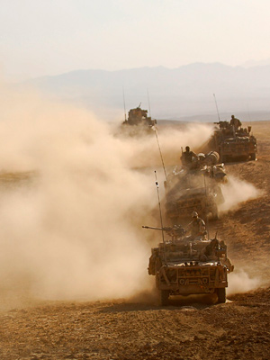 A convoy of land vehicles drive across a desert.