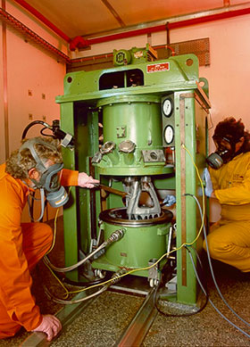 Two scientists in protective clothing handling insensitive munitions.