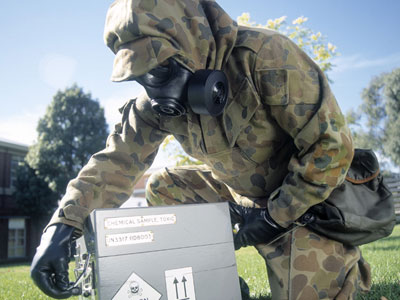 An image of a person wearing protective clothing handling a box containing hazardous materials.