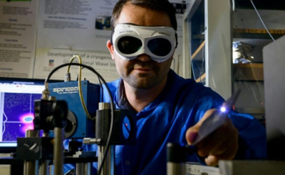 Miftar Ganija, wearing goggles investigates short pulsed laser systems in the lab.
