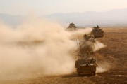 A convoy of land vehicles drive across a desert.