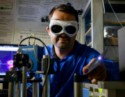 Miftar Ganija, wearing goggles investigates short pulsed laser systems in the lab.