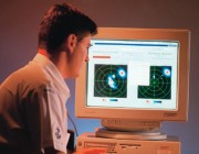 A photograph of a man looking at a computer screen displaying MEXANS Geographic Information Systems