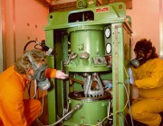 Two scientists in protective clothing handling insensitive munitions.