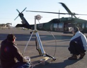 Men using GPS equipment in front of a helicopter
