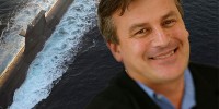 Dr Alex Zelinsky in front of a large photograph of a submarine.